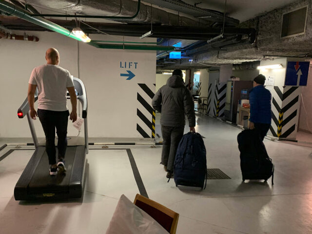 En mann går på en tredemølle. To andre menn går med trillebagger.