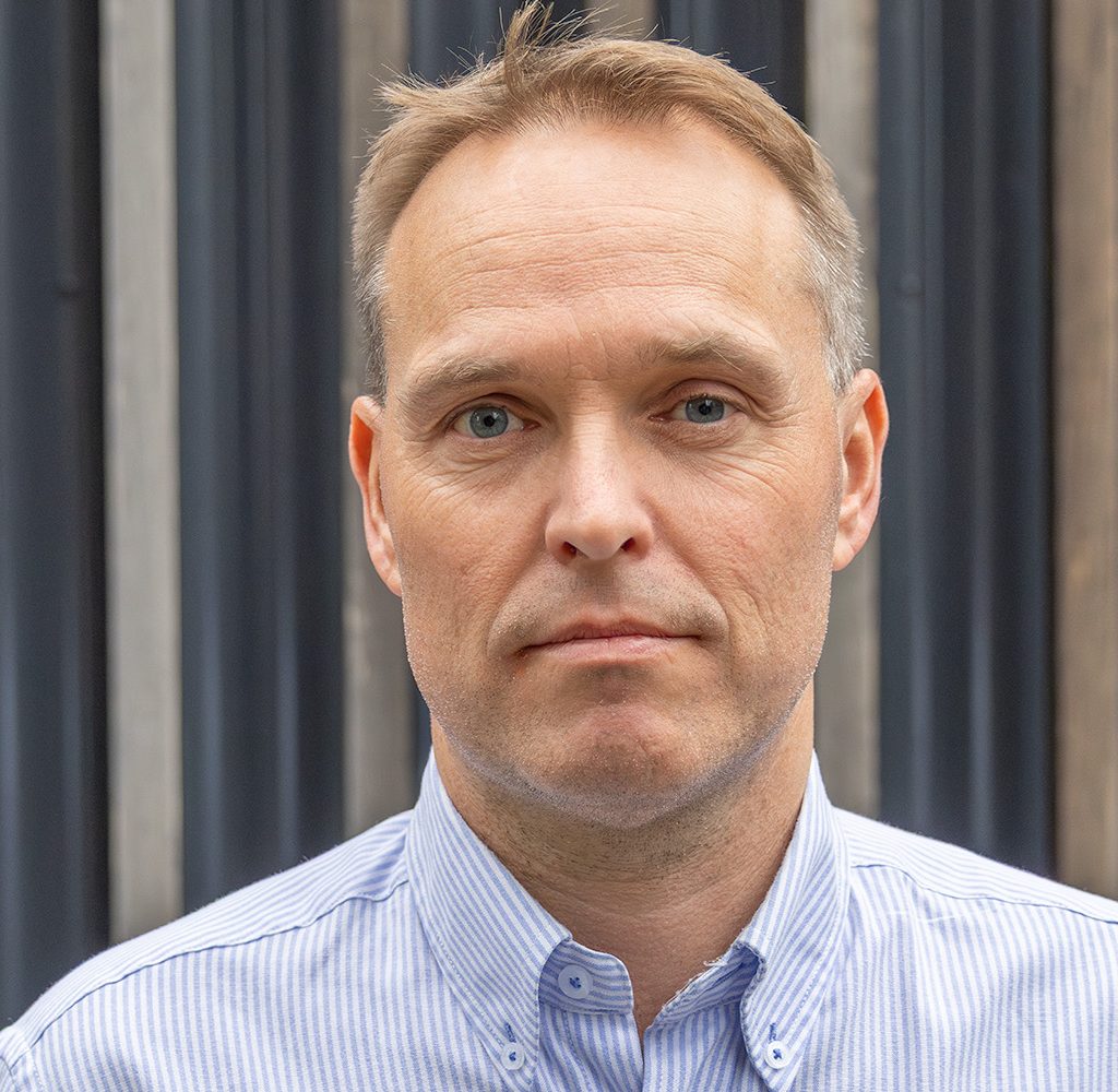 Mann i blåstripete skjorte ser rett i kameraet.