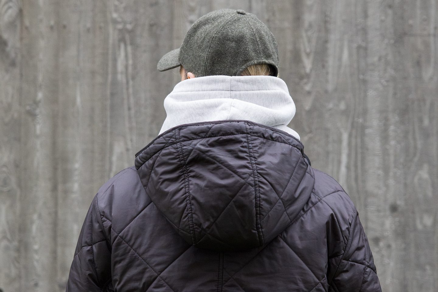 Kvinne med hettegenser og boblejakke sett bakfra. Hun ser inn i en vegg.