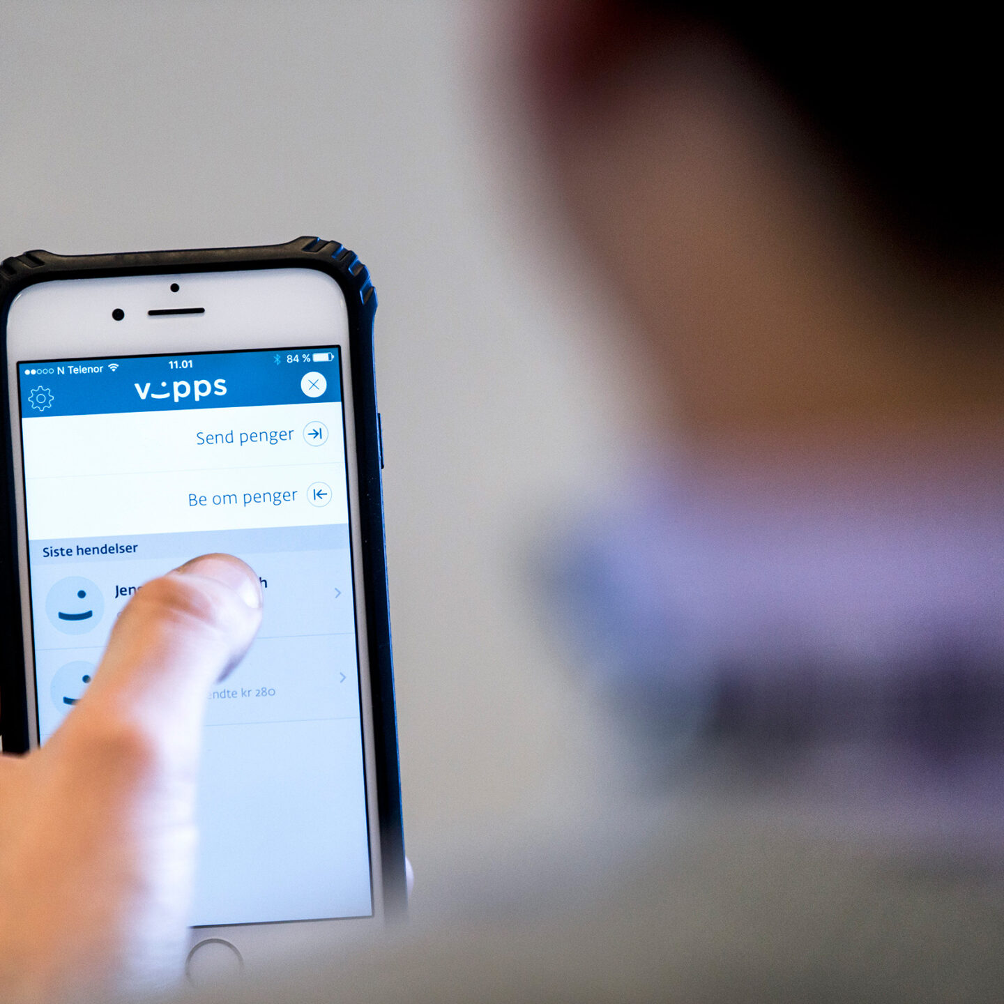 Mann ser på en mobiltelefon. På skjermen er et bilde av Vipps.