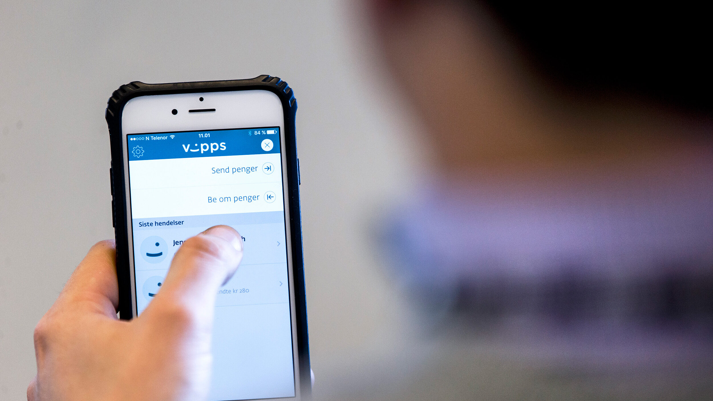 Mann ser på en mobiltelefon. På skjermen er et bilde av Vipps.