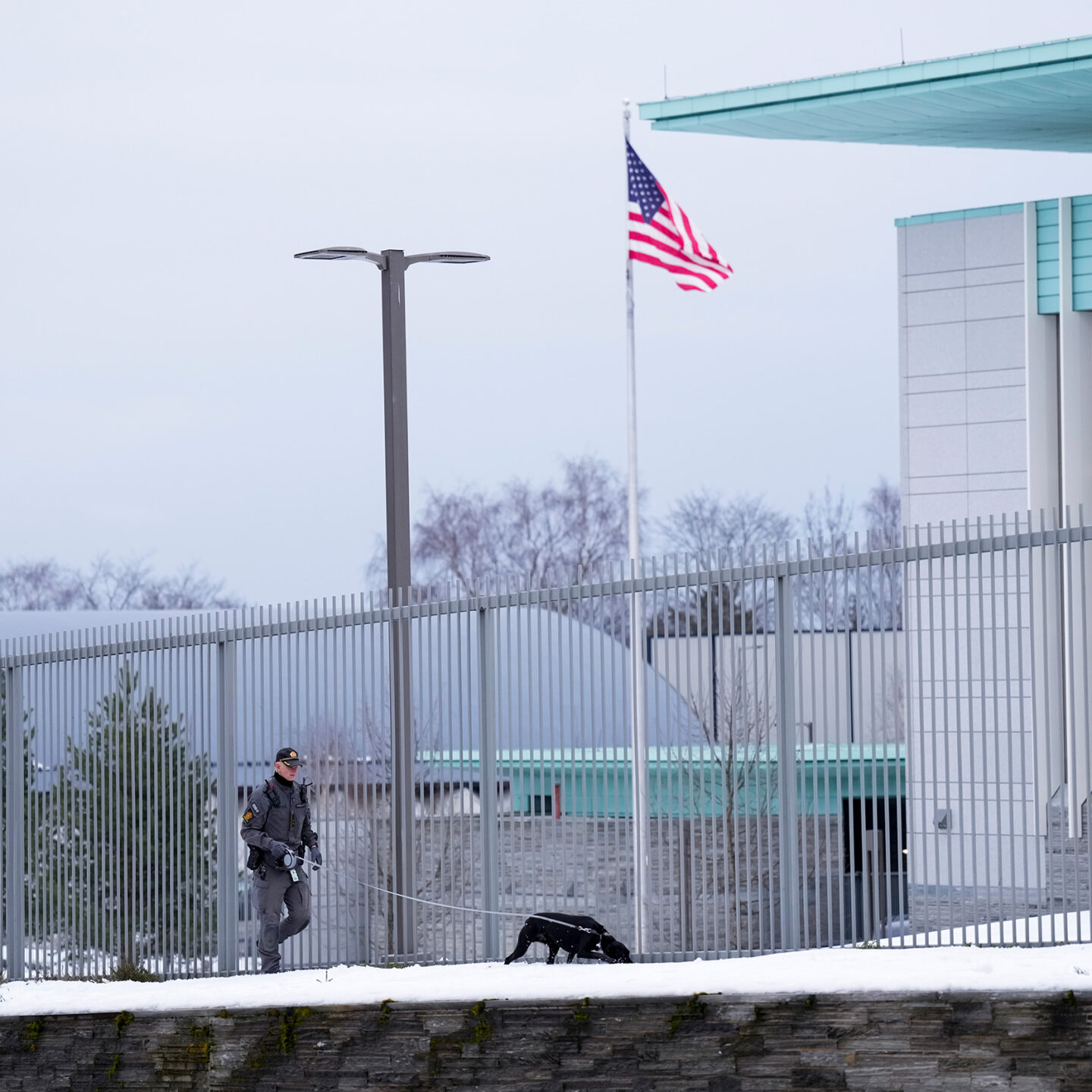 Politimann med en hund i bånd. Utenfor den amerikanske ambassaden. Foto.