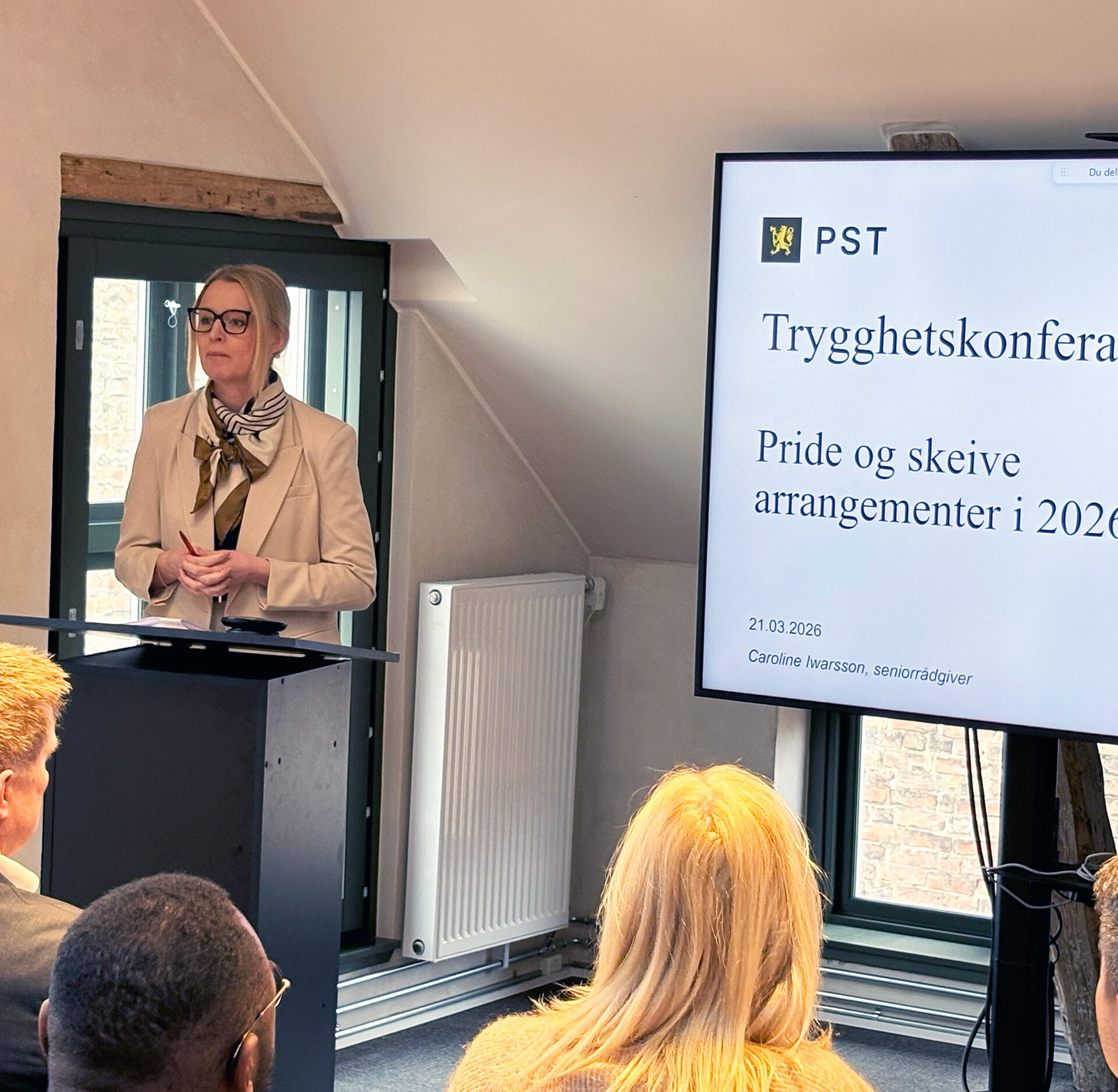 Kvinne stående på en scene. Presenterer innhold på en skjerm. Foto.