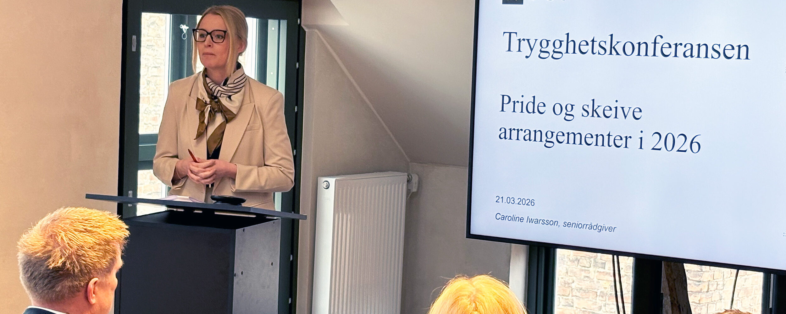 Kvinne stående på en scene. Presenterer innhold på en skjerm. Foto.