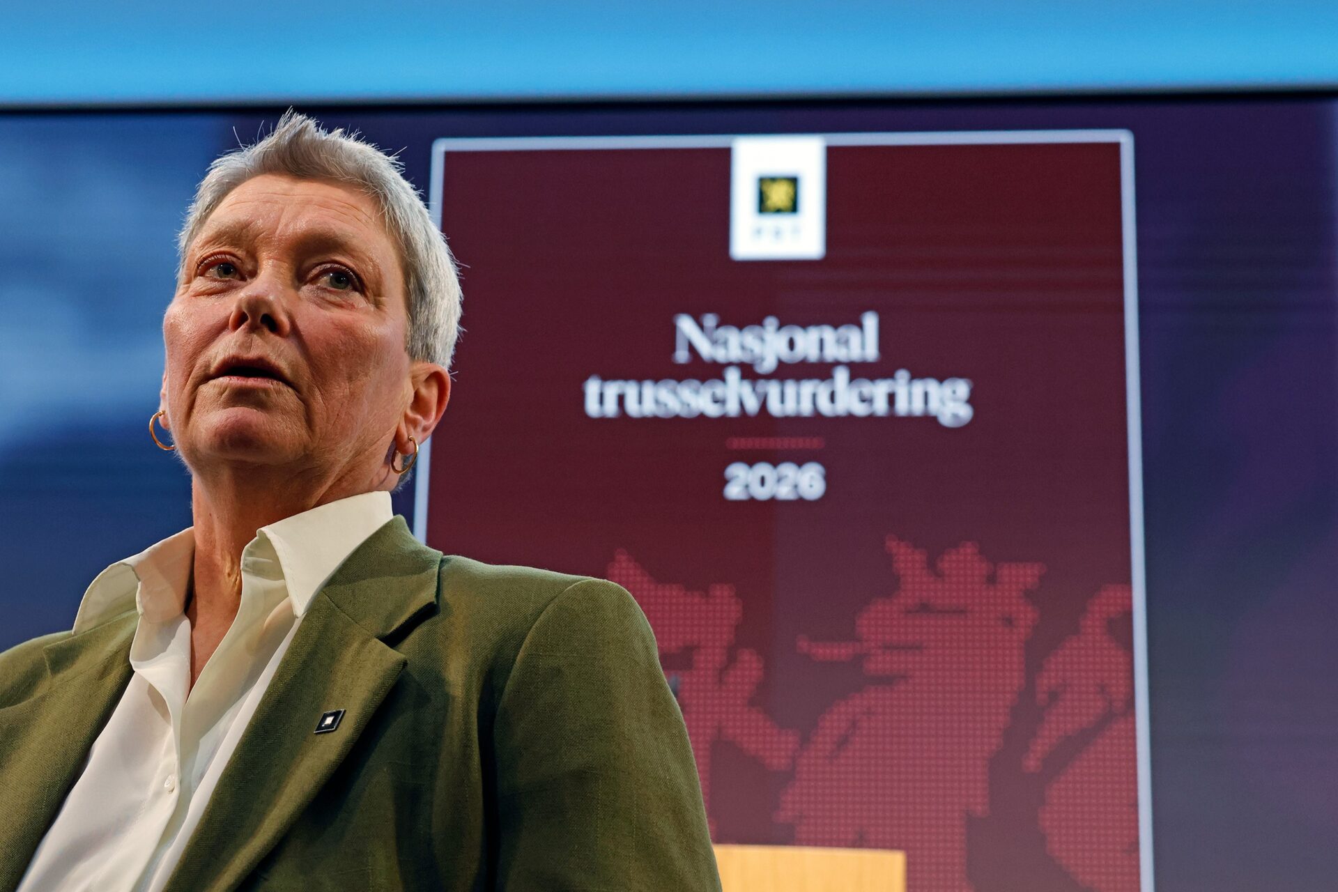 Sjef PST, Beate Gangås, står foran en skjerm som viser forsiden av PSTs nasjonale trusselvurdering 2026.Foto
