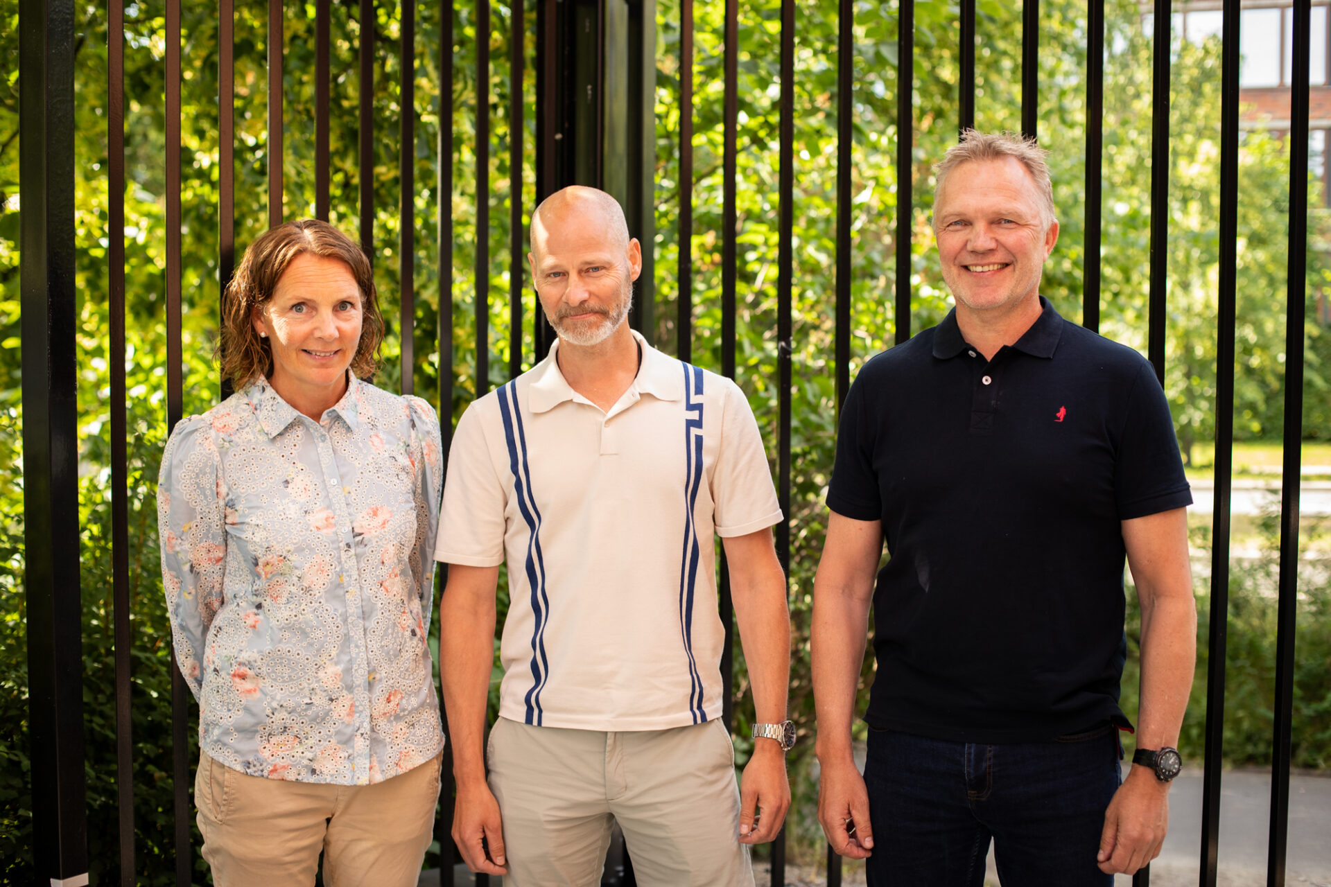 Gruppebilde av Kristin (Den kongelige politieskorte, PST), Christian (Beskyttelse av myndighetspersoner, PST) og Gisle (Politihøgskolen) som står foran et svart gjerde en fin sommerdag